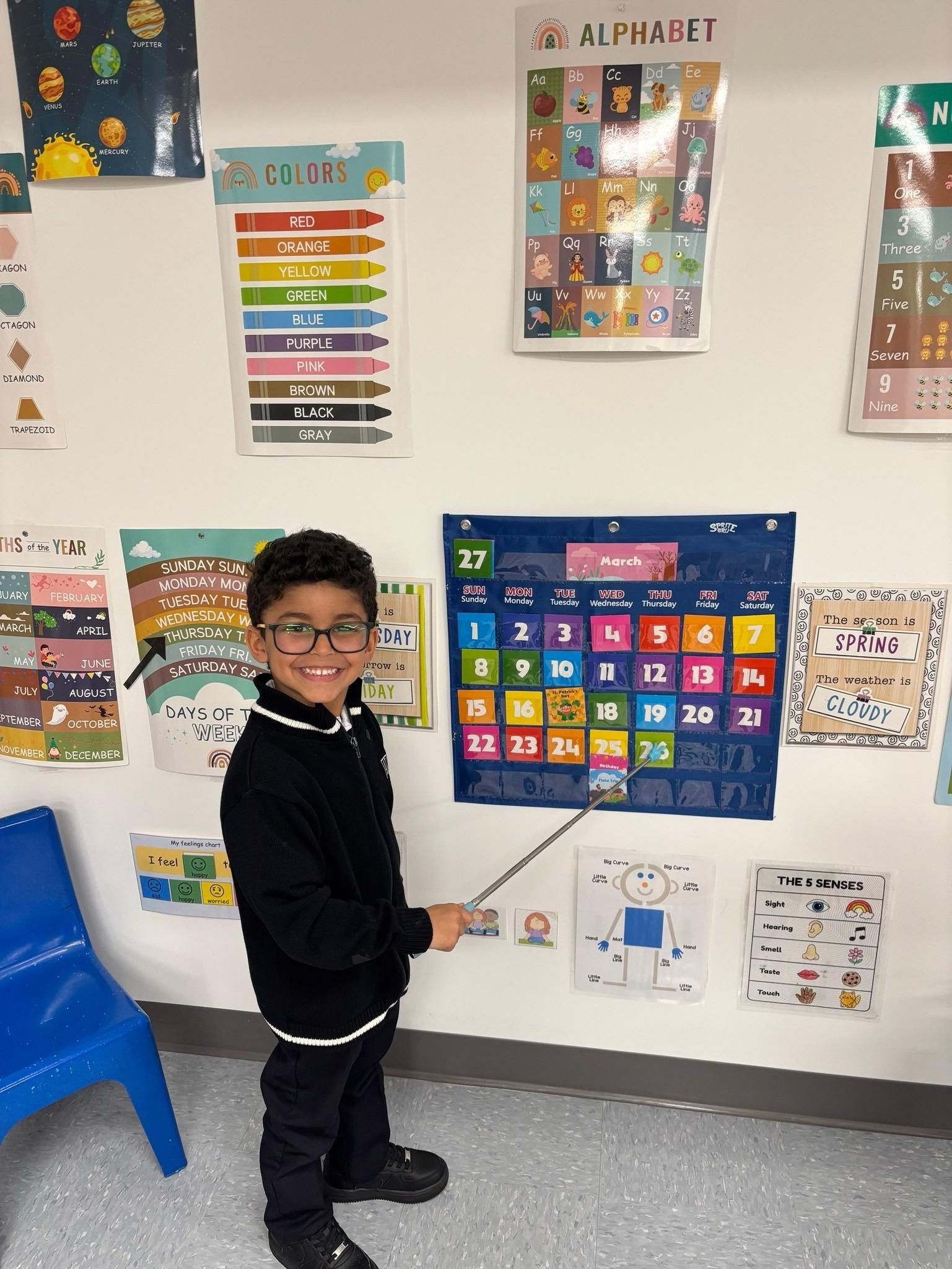 Un élève de maternelle 4 ans devant le calendrier de la classe, entouré d'affiches en français et en anglais