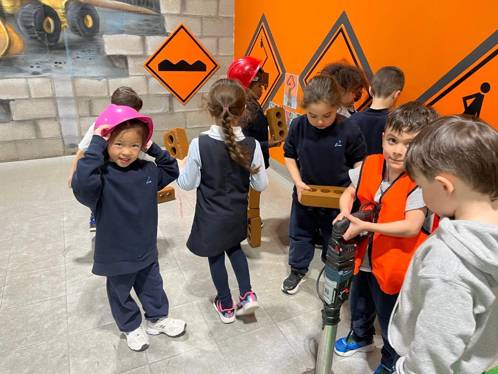 Élèves de maternelle 4 ans en sortie scolaire, casques de chantier sur la tête, explorant un atelier de construction