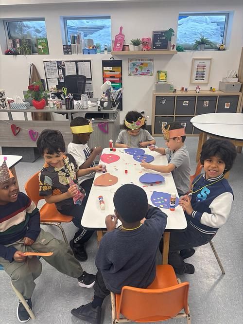 Élèves de maternelle 5 ans réunis autour d'une table pour un bricolage, couronnes de papier sur la tête