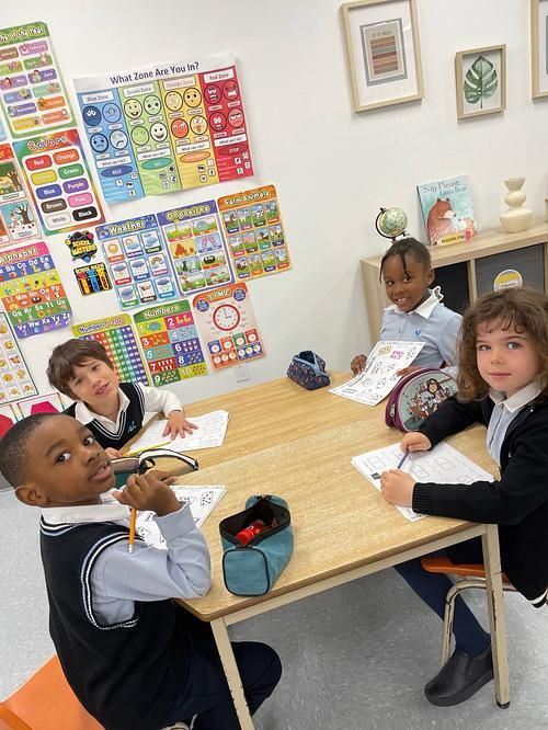 Élèves de maternelle 5 ans à leur table de travail, devant un mur d'affiches en français et en anglais