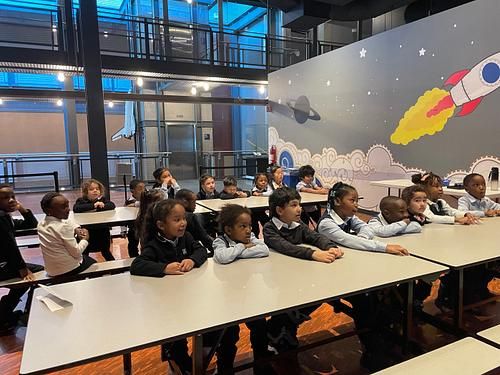 Élèves de maternelle 5 ans attentifs lors d'une sortie scolaire, devant une murale de fusée