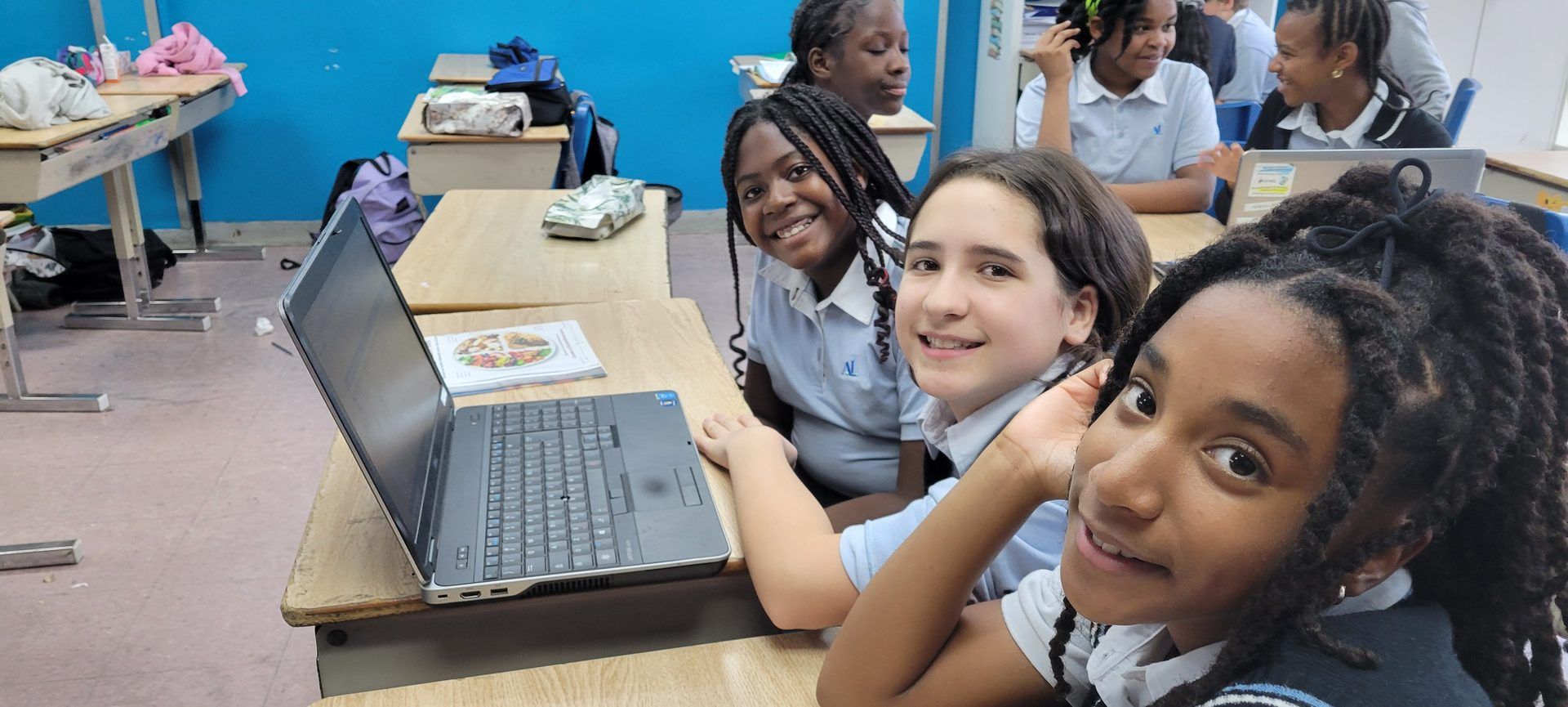 Élèves du primaire souriants autour d'un ordinateur portable de l'école